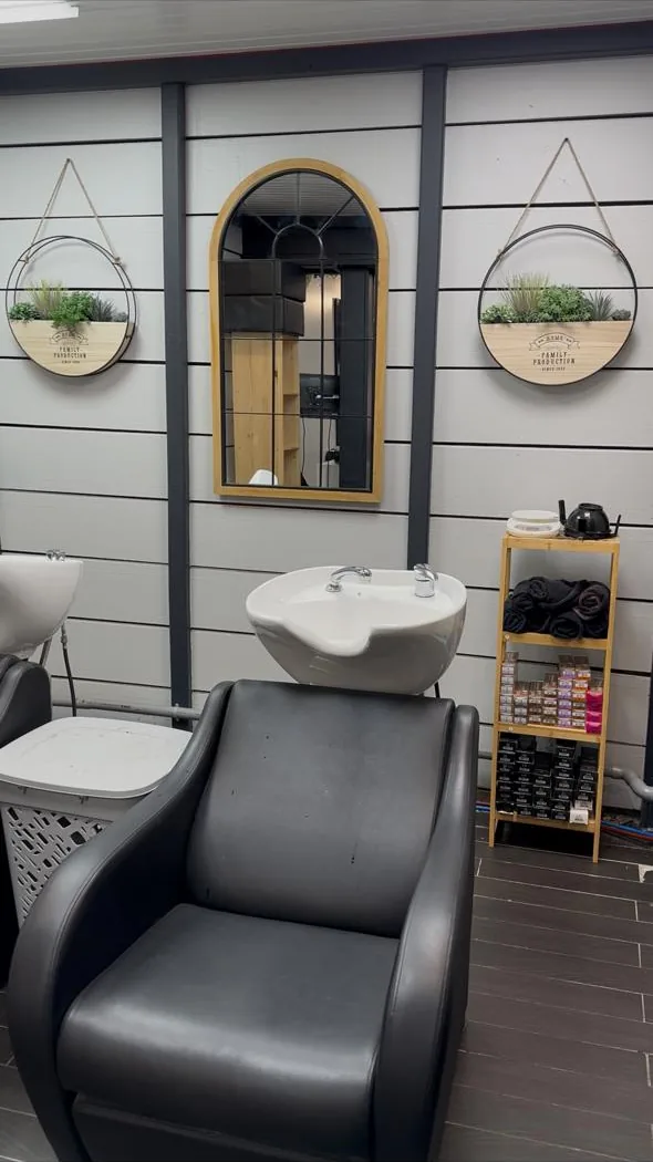 Bac à shampoing du salon devant un mur en lambris blanc, entre deux miroirs ronds à sangle