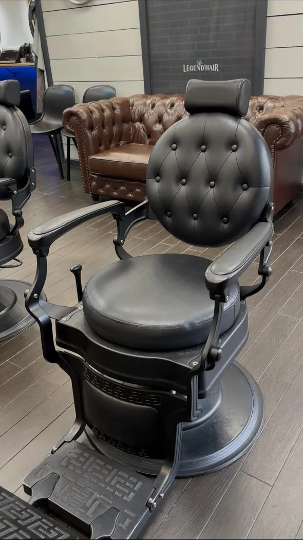 Fauteuil de barbier en fonte au dossier de cuir noir capitonné, devant les canapés Chesterfield cognac du salon