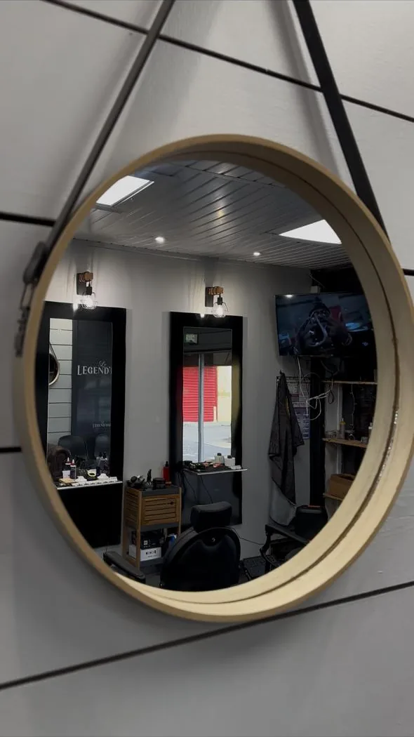 Miroir rond à cadre de bois clair suspendu à une sangle, reflétant la salle du Legend'Hair